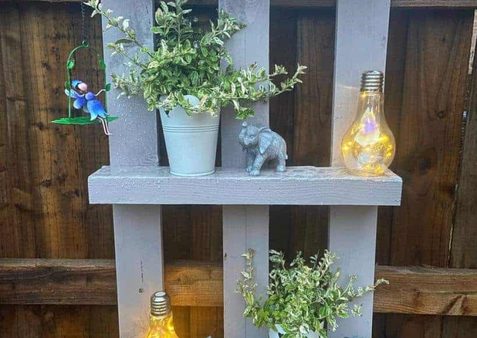 A wooden pallet shelf with potted plants and lights.