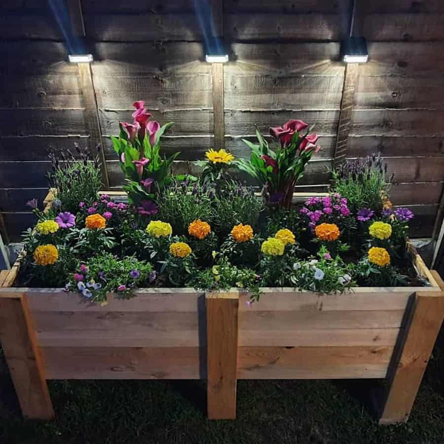 A wooden planter with flowers in it at night.